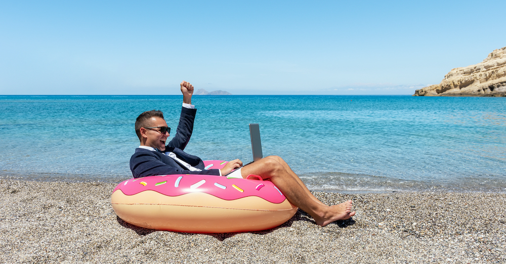 Happy businessman with laptop on inflatable donut on tropical beach. Summer vacation concept.